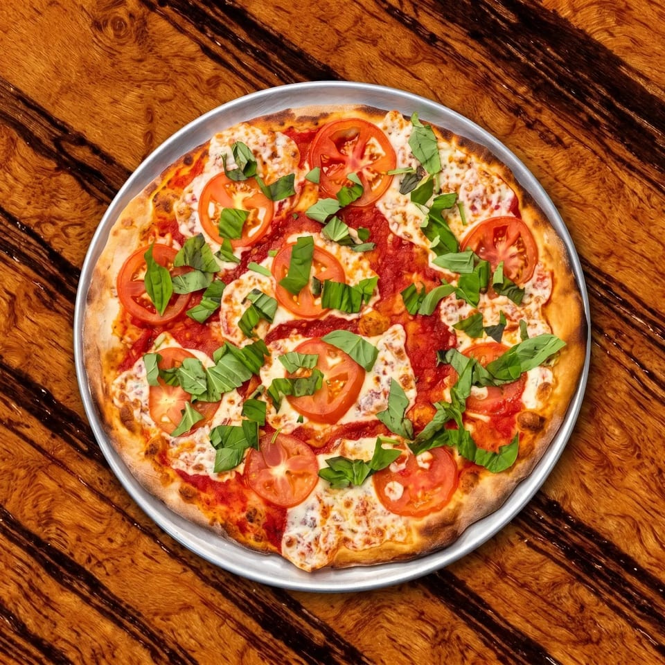 Margherita pizza topped with melted cheese, sliced tomatoes, and fresh basil on a metal tray atop a wooden table.